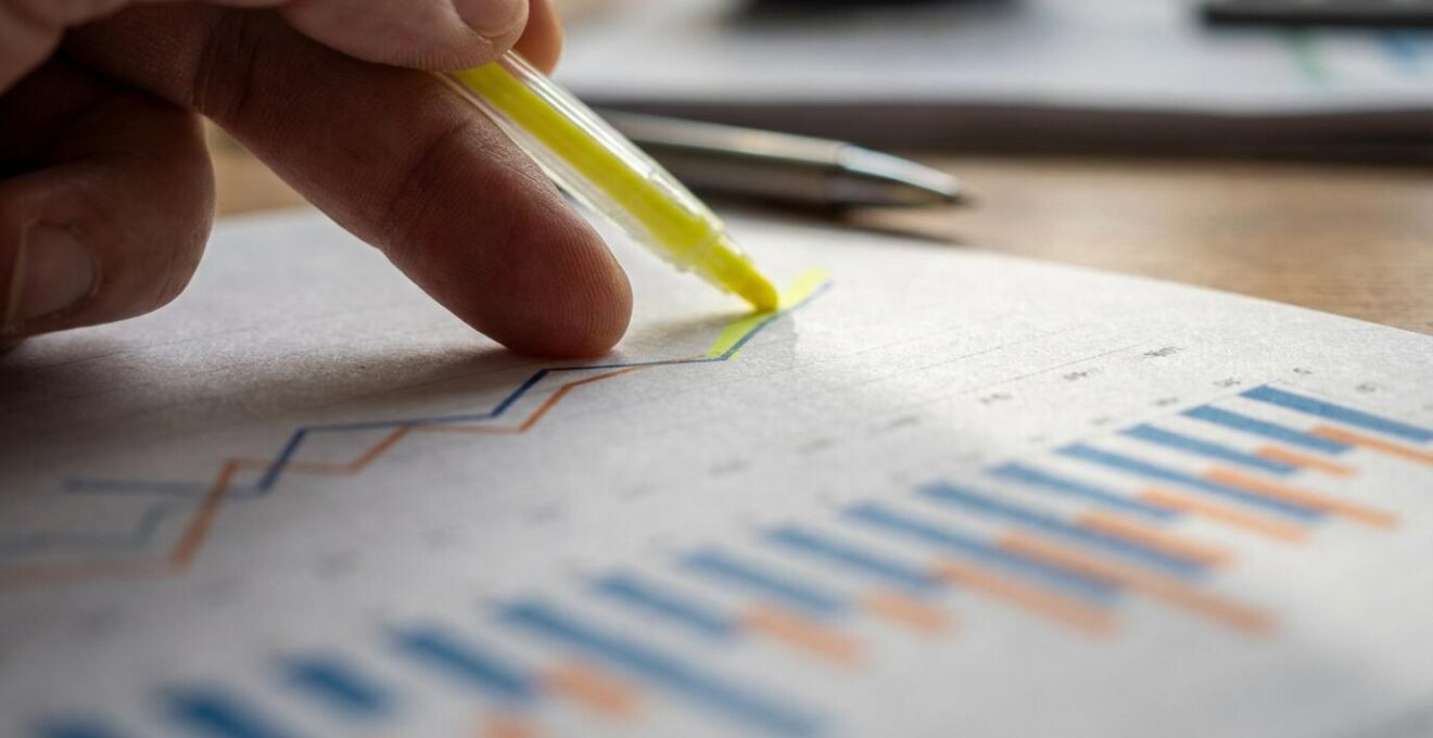 Hands analyzing printed charts and graphs showing market trends with highlighting markers
